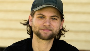 Image of a young white man wearing a baseball cap and smiling at the camera.